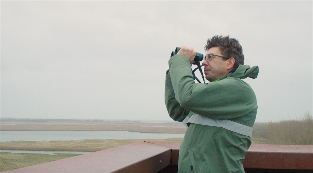 Man met verrekijker kijkt uit over Lauwersmeer