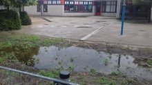 Bioswale on a school playground. On the front you see a puddle of water on a piece of grass. Behind this, there is the playground visible.
