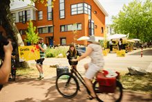 Vrijwilliger houdt bord "Gratis ijs" omhoog, terwijl bezoekers op de fiets langsrijden op een buurtevenement.